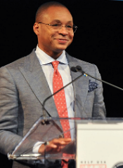 Gus Johnson speaking at a podium.